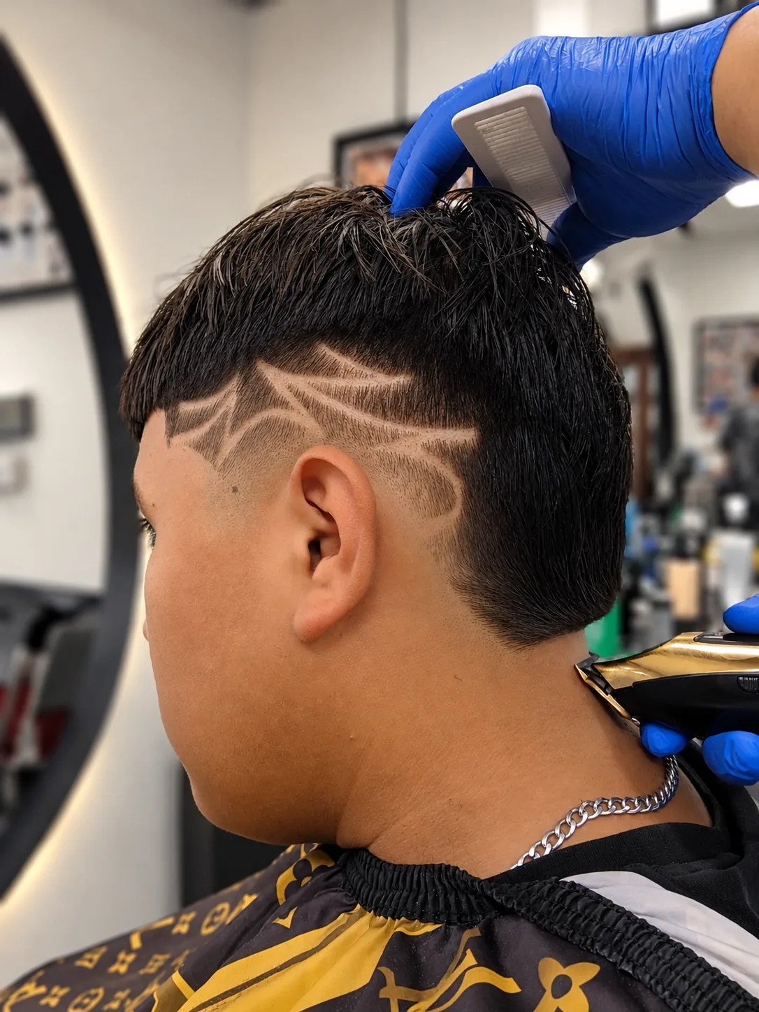 Barbero perfilando un diseño con la máquina en la nuca de un cliente